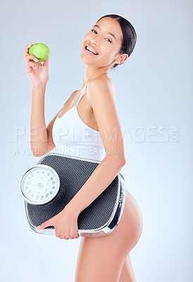 Buy stock photo Studio shot of a young woman tossing an apple while holding a scale against a grey background