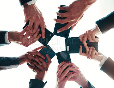 Buy stock photo Low angle shot of a group of unrecognisable businesspeople using their cellphones while standing in a huddle