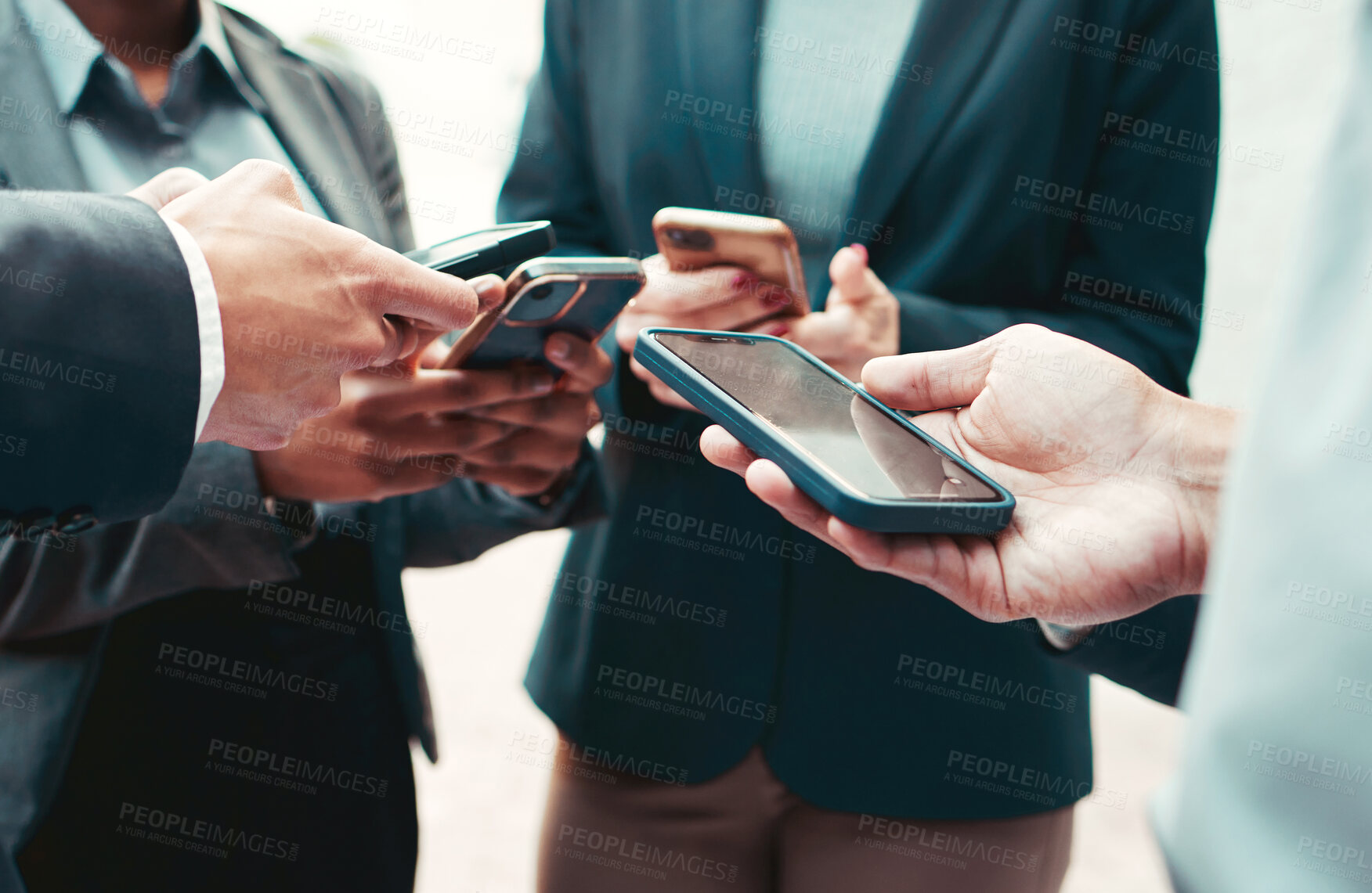 Buy stock photo High angle shot of a group of unrecognisable businesspeople using their cellphones while standing in a huddle