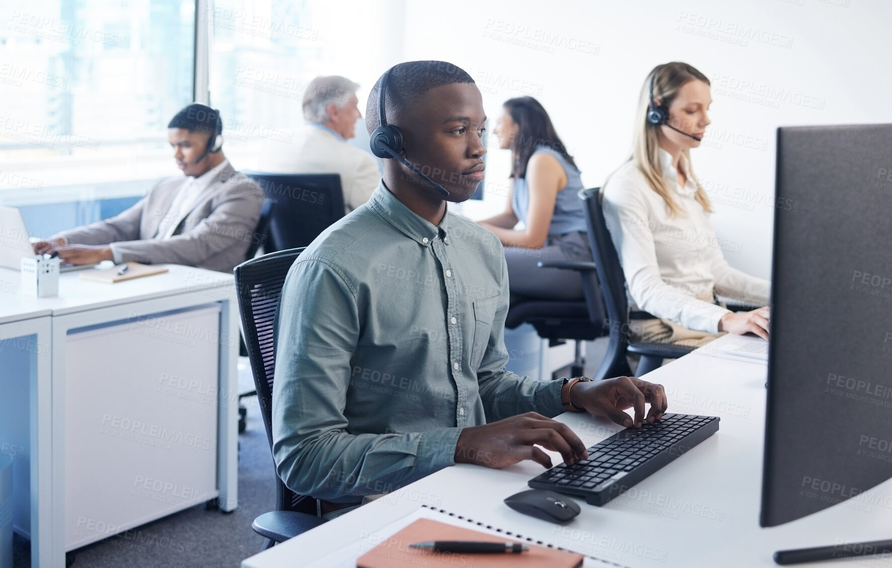 Buy stock photo Shot of a young businessman using a headset and computer in a modern office