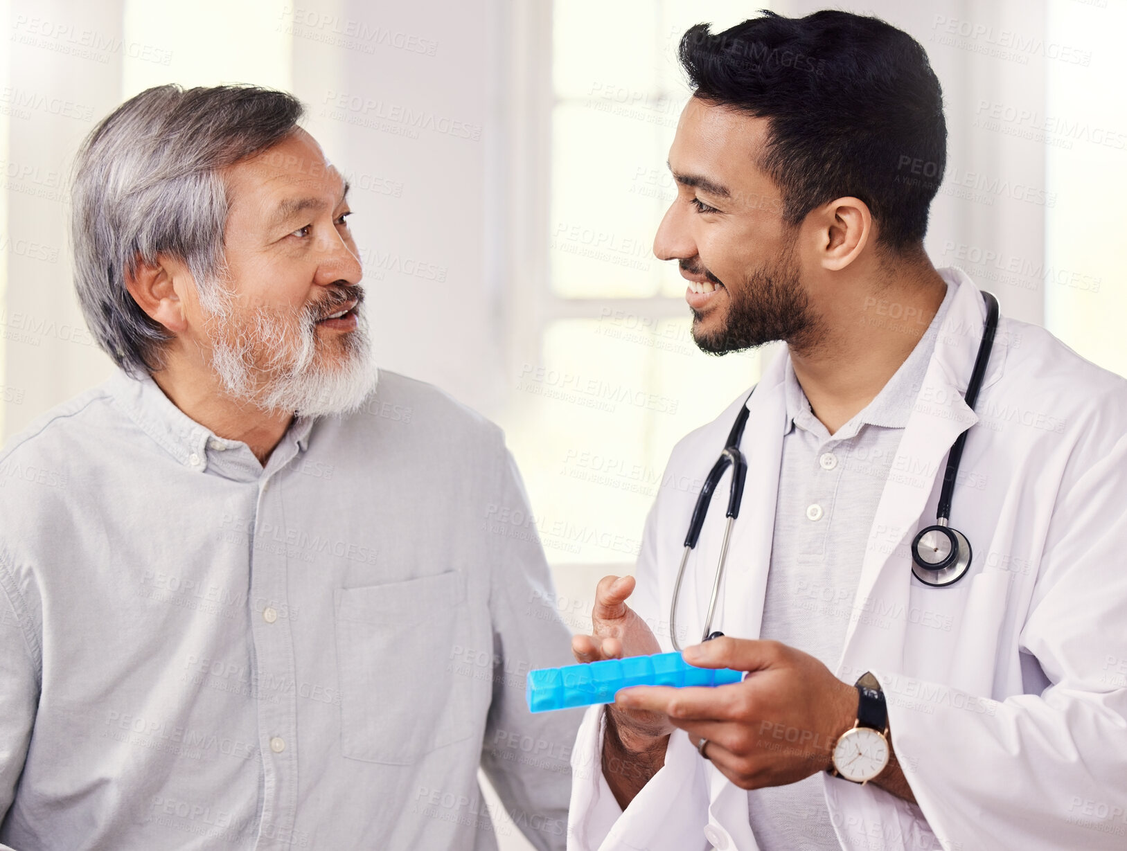 Buy stock photo Shot of a doctor holding a pill box while talking to a senior patient