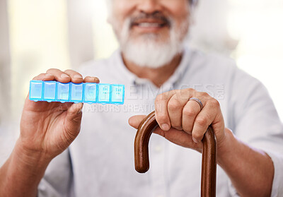Buy stock photo Shot of a senior man sitting with a walking stick and holding up a weekly pill box