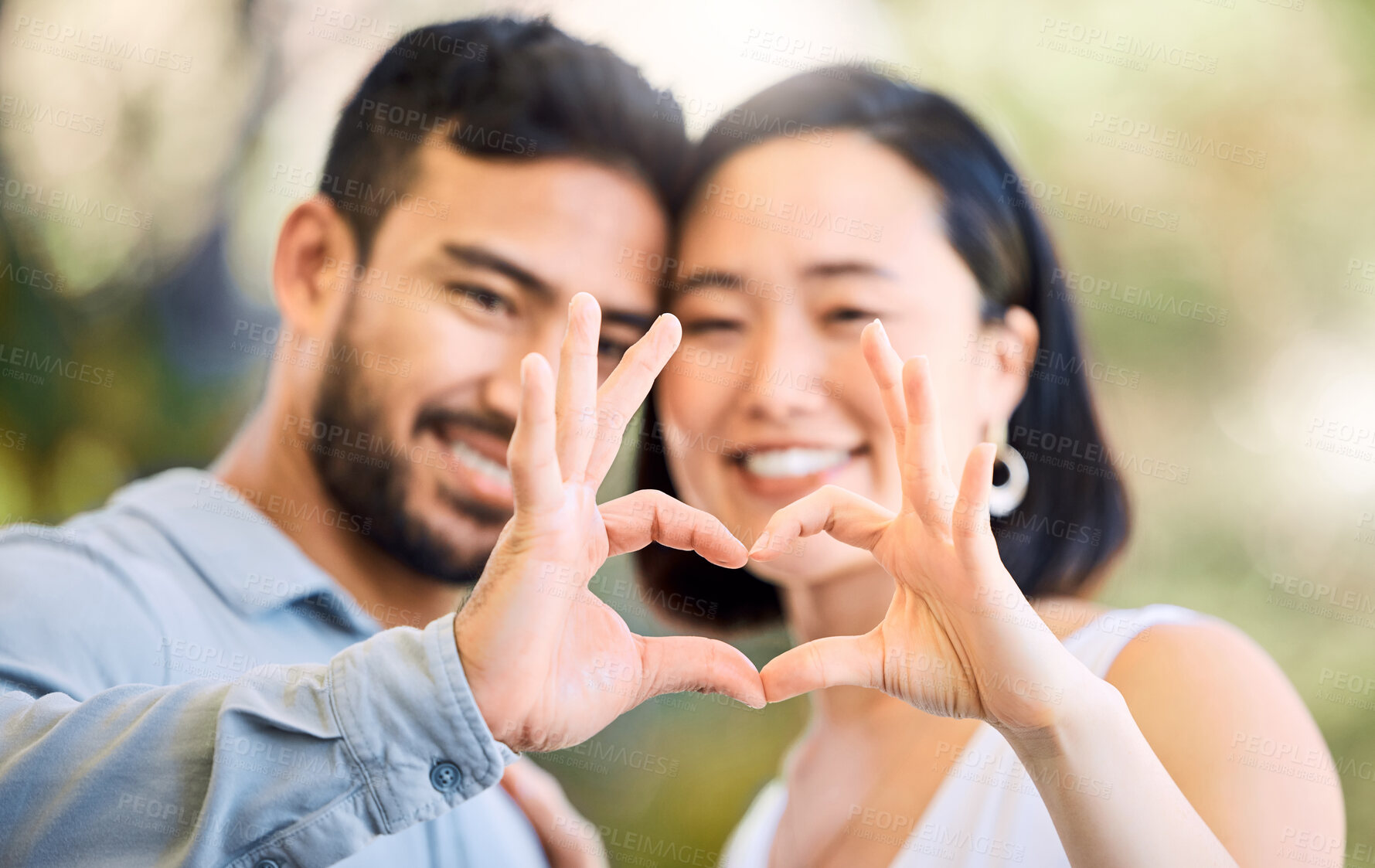 Buy stock photo Shot of a happy young couple making a heart shaped gesture in a garden