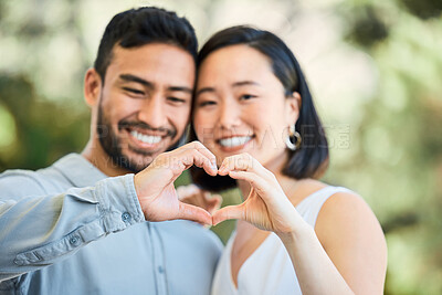 Buy stock photo Shot of a happy young couple making a heart shaped gesture in a garden