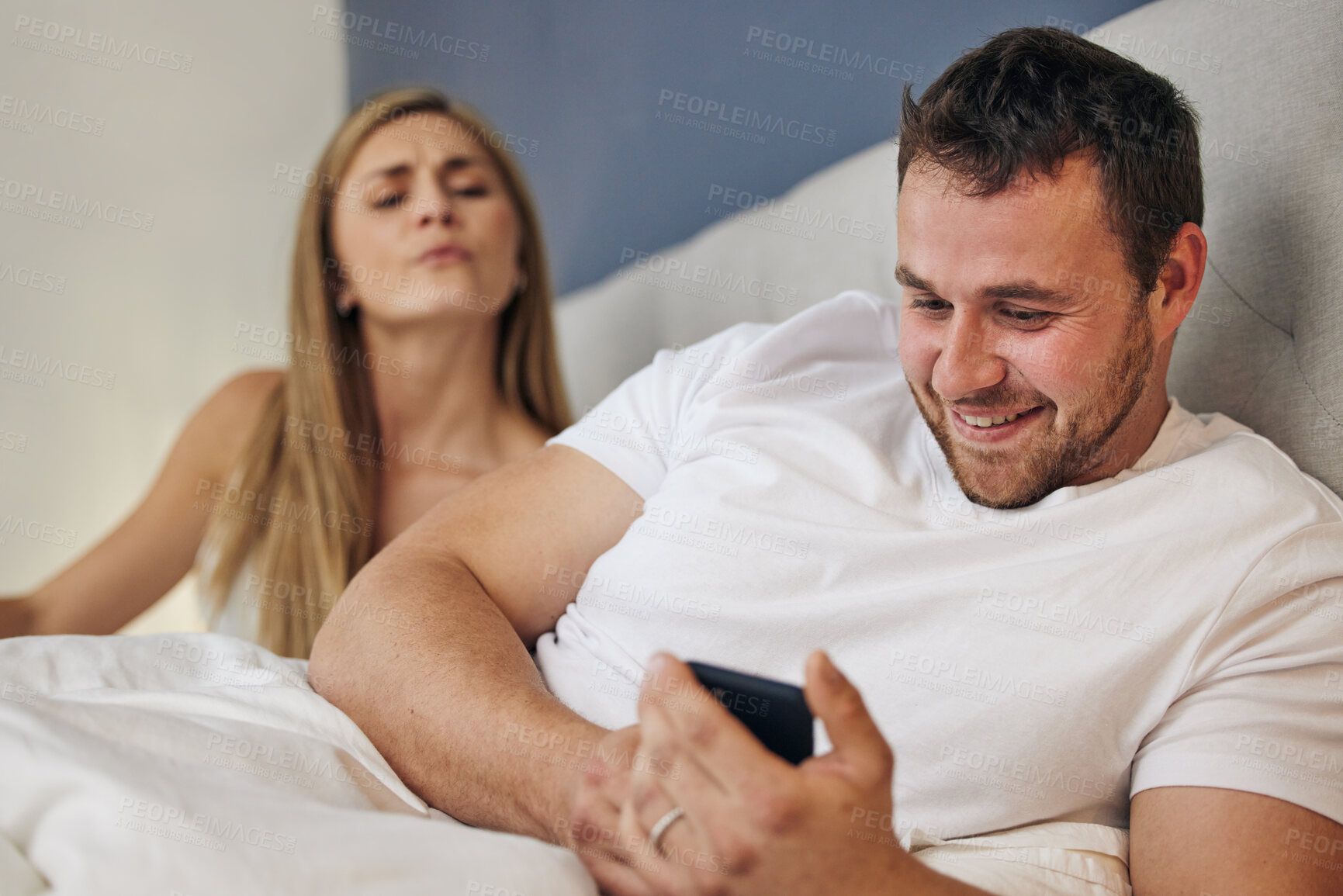 Buy stock photo Phone, bed and man with angry wife for cheating, infidelity or affair communication online at home. Marriage conflict, argument and happy male person network on cellphone with upset woman in bedroom.