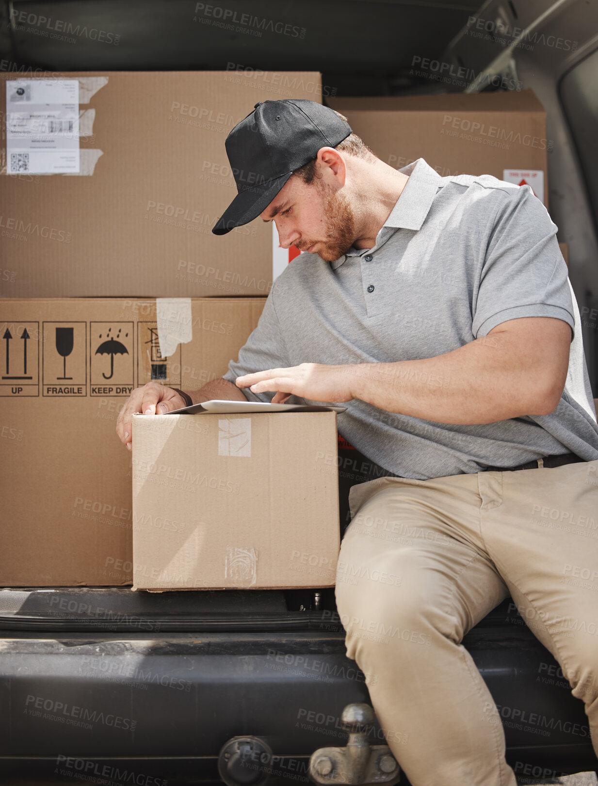 Buy stock photo Cropped shot of a handsome young delivery man using a tablet while sitting in the back of his van