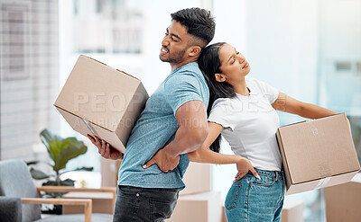 Buy stock photo Shot of a young couple standing and suffering from backache while carrying boxes in their new home