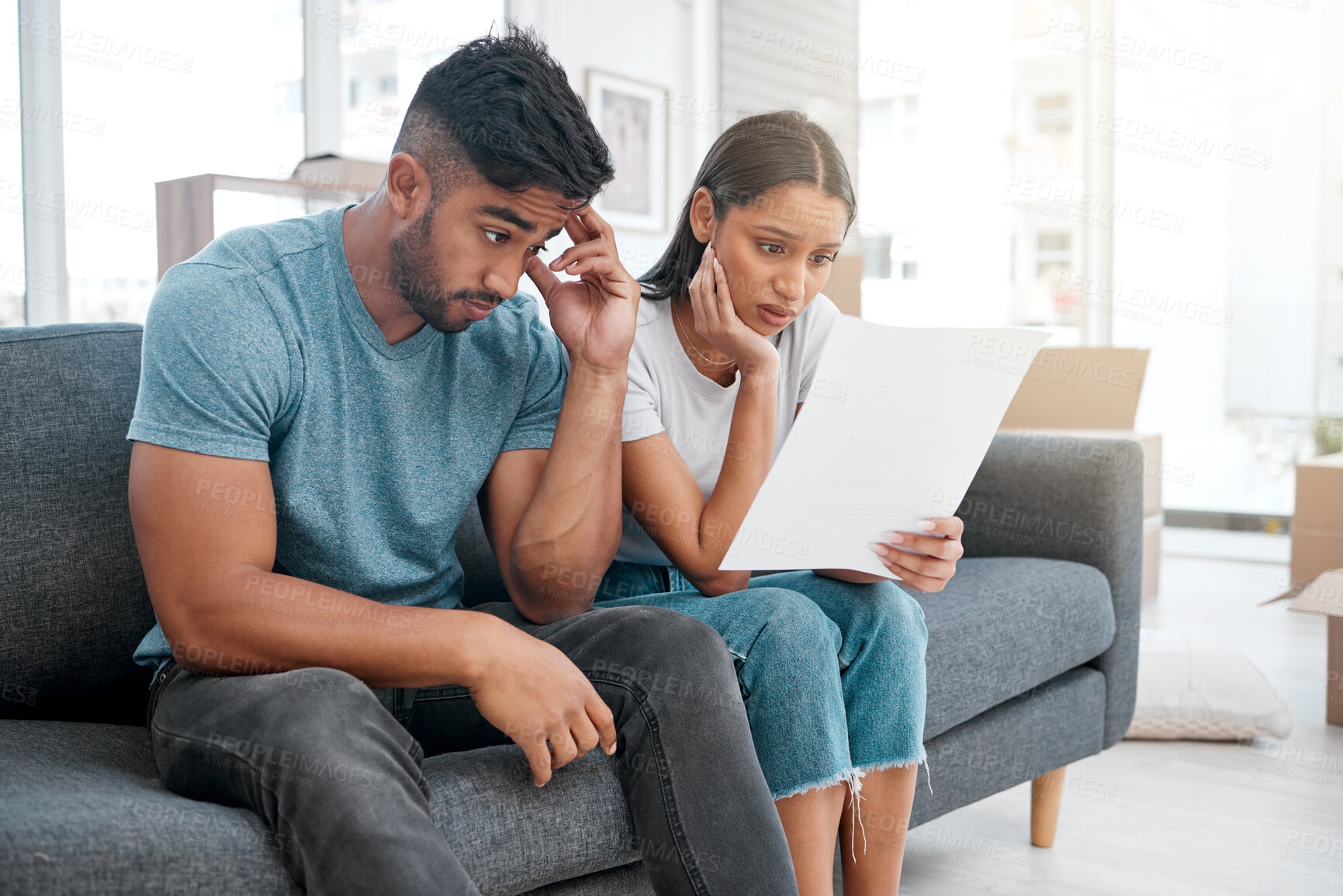Buy stock photo Shot of a young couple sitting on the sofa at home and feeling stressed after receiving an eviction notice