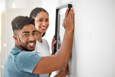 Buy stock photo Shot of a young couple putting a picture frame up on their wall in their new home