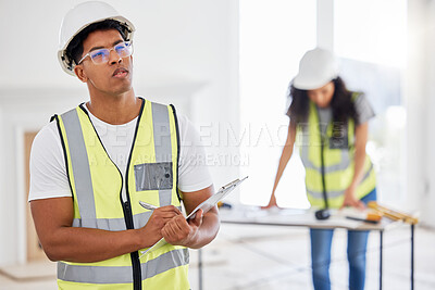 Buy stock photo Shot of a handsome young contractor standing inside and looking contemplative while using a clipboard