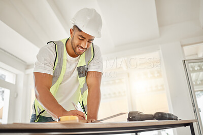 Buy stock photo Shot of a handsome young construction worker standing alone inside and drawing up building plans
