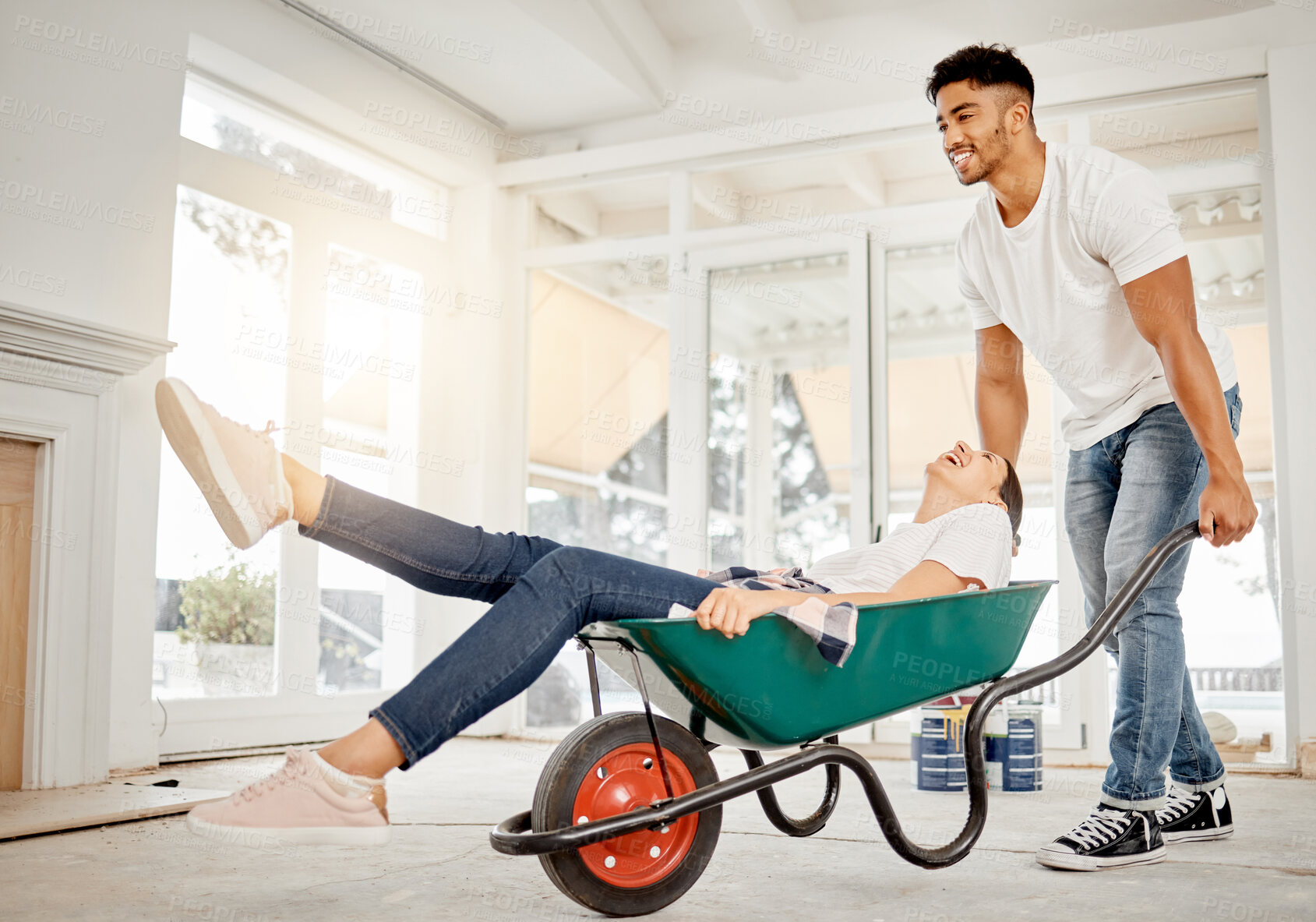 Buy stock photo Happy couple, wheelbarrow and moving in with new home for renovation, building or DIY restoration. Young man and woman with smile for fun relocation, interior design or architecture together at house