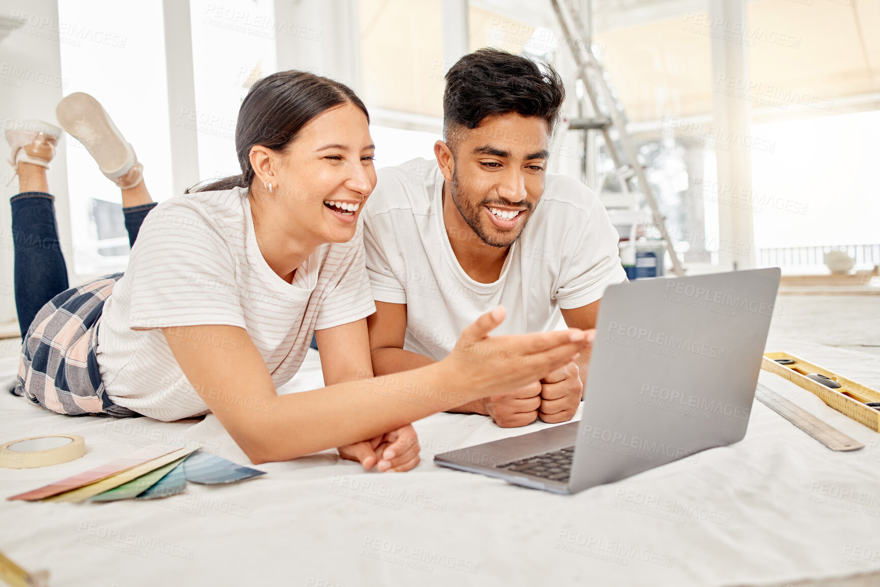 Buy stock photo Shot of a young couple lying on their living room floor and using a laptop