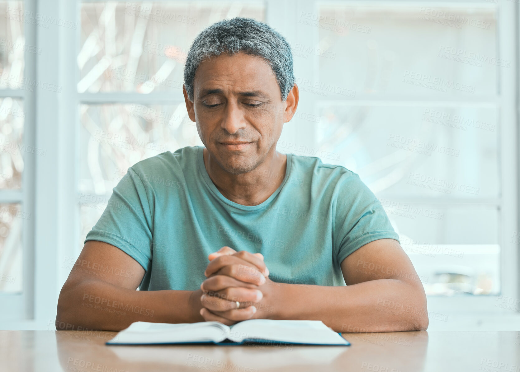 Buy stock photo Senior, man and praying with bible in home with worship, spiritual practice and gratitude at table. Christianity, mature person and holy book for praise to God, forgiveness or thankful in living room