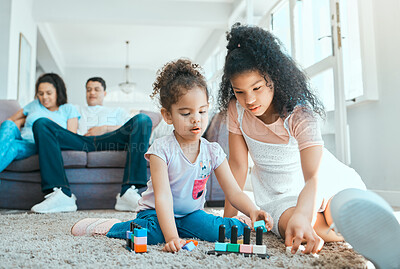 Buy stock photo Shot of two sister playing on the floor while their parents relax in the background