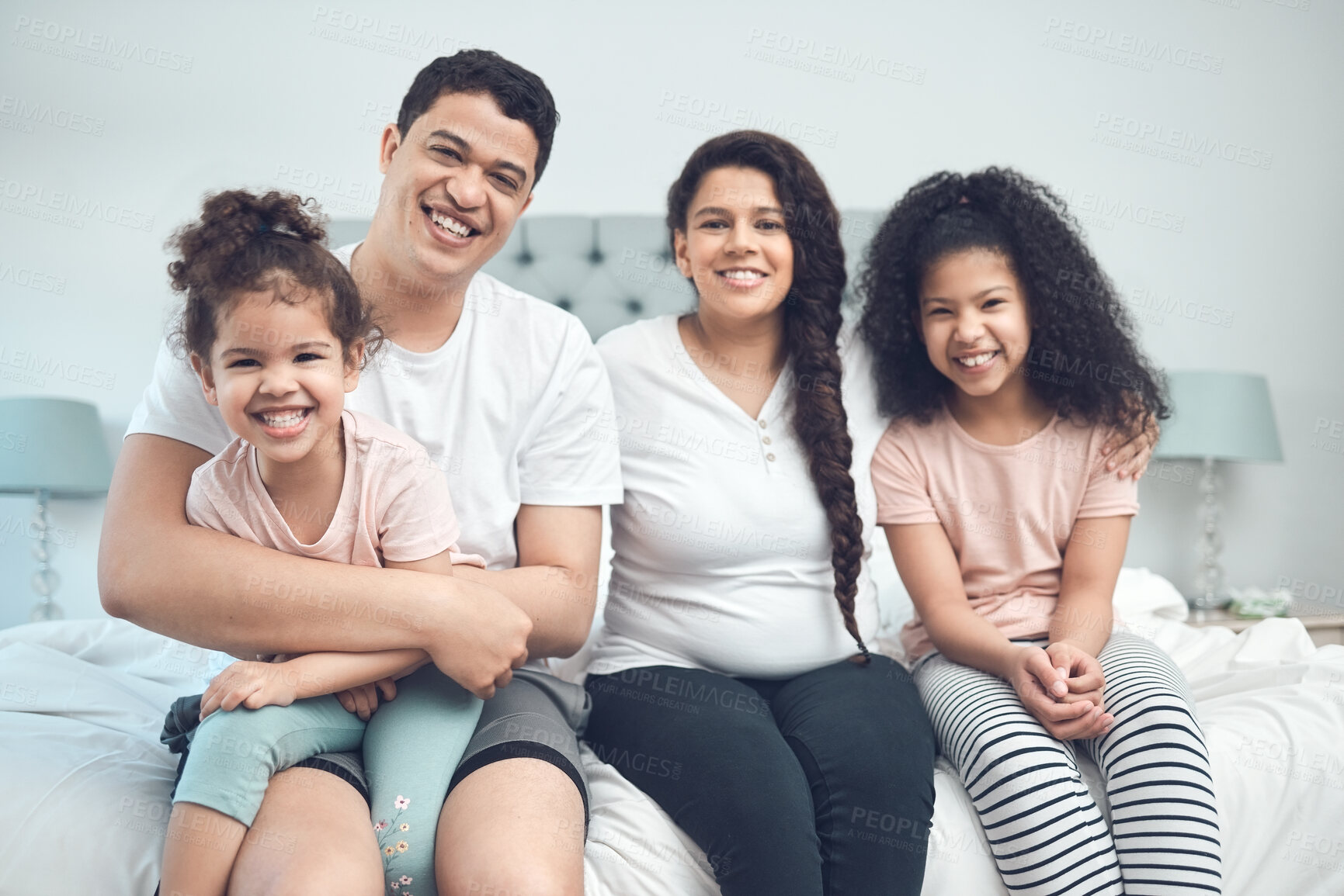 Buy stock photo Portrait of a beautiful young family talking and bonding while sitting on a bed together