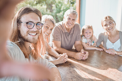 Buy stock photo Shot of a handsome young man sitting with his family and taking selfies