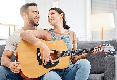 Buy stock photo Shot of a young couple playing guitar while relaxing together on a sofa at home