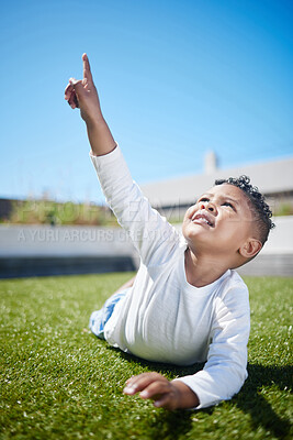 Buy stock photo Shot of a little boy pointing to the sky while lying on the grass outside