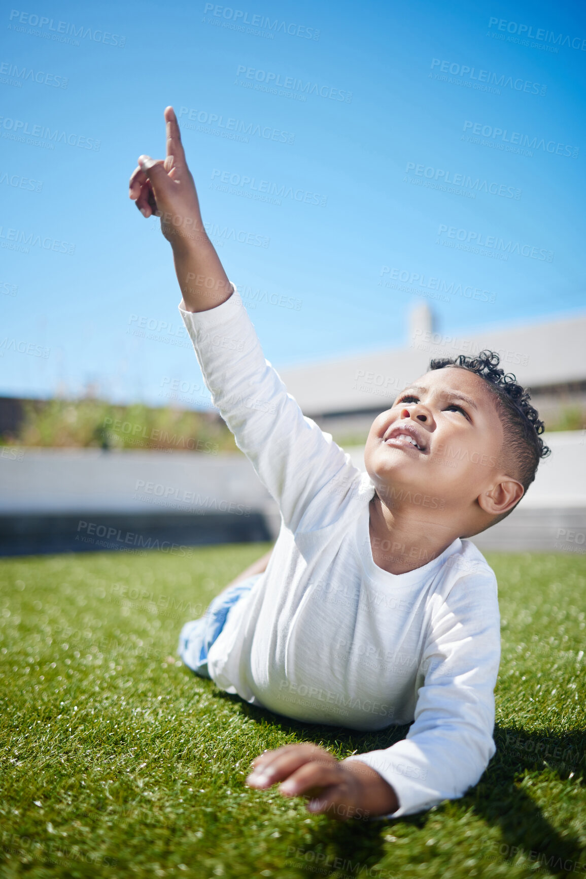 Buy stock photo Shot of a little boy pointing to the sky while lying on the grass outside