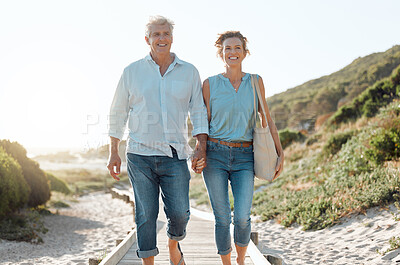 Buy stock photo Senior, couple and walking at the beach with hands in portrait for happiness on a vacation in the outdoor. Mature, woman and man holding by ocean for travel on holiday with sunshine for the weekend.