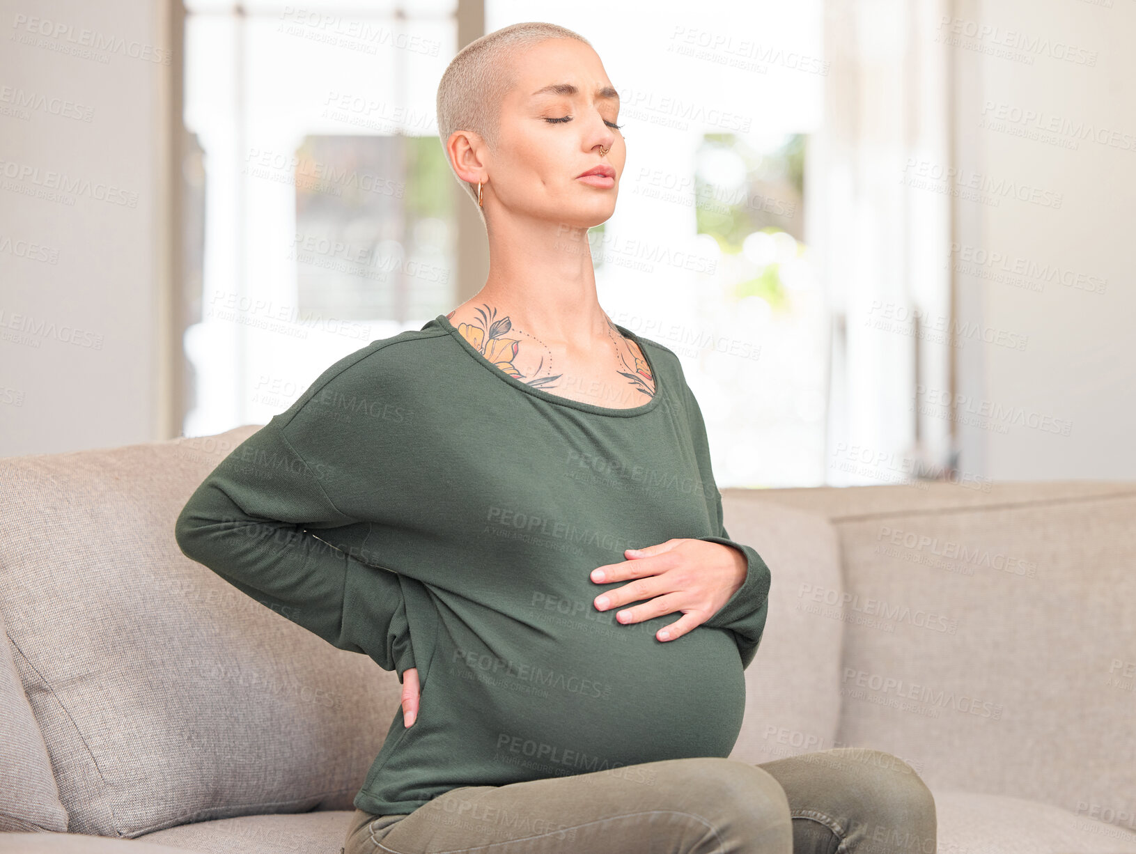 Buy stock photo Cropped shot of an attractive young pregnant woman looking uncomfortable while sitting on the sofa at home