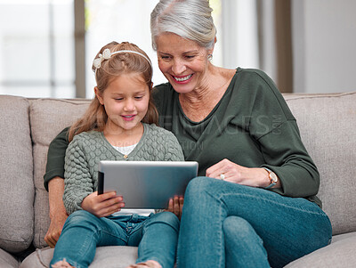 Buy stock photo Shot of a grandmother and granddaughter bonding on the sofa while using a digital tablet
