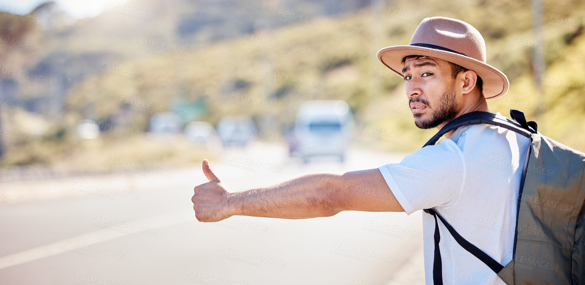 Buy stock photo Shot of a young man hitchhiking on the side of the road