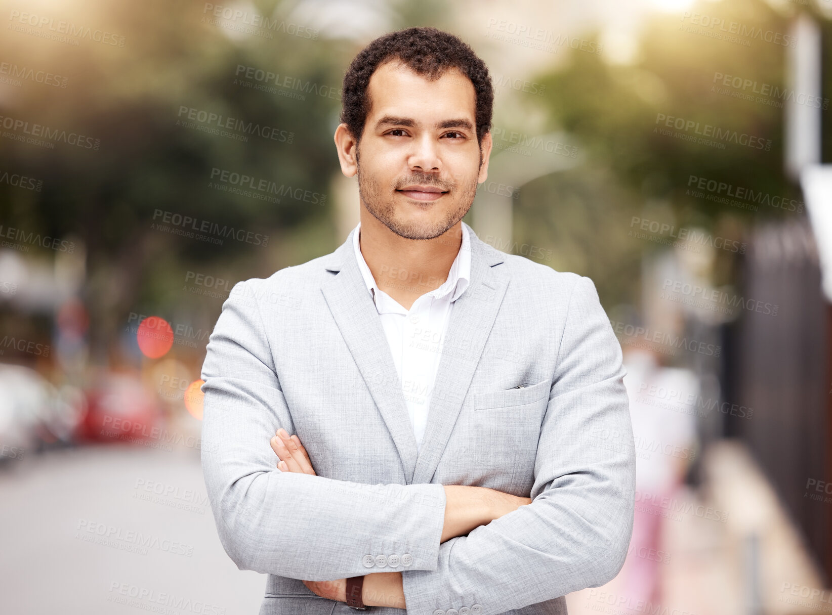 Buy stock photo Shot of a young businessman standing with his arms crossed against a city background