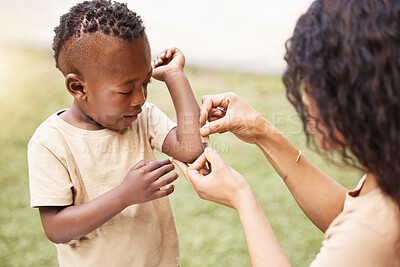 Buy stock photo Shot of a mother applying a bandaid to her son's arm outside