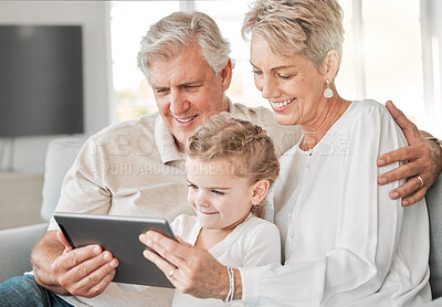 Buy stock photo Shot of an adorable little girl using a digital tablet while sitting at home with her grandparents
