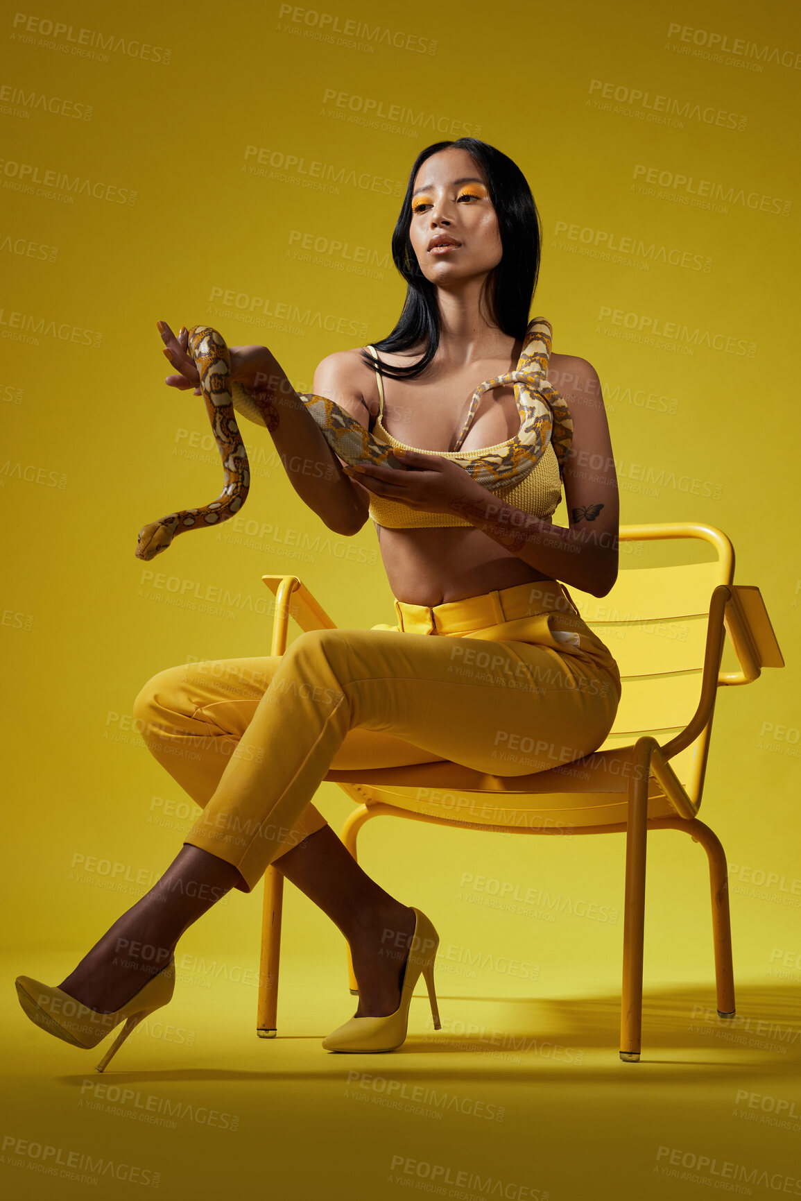 Buy stock photo Shot of a fashionable woman holding a snake while modelling a yellow concept