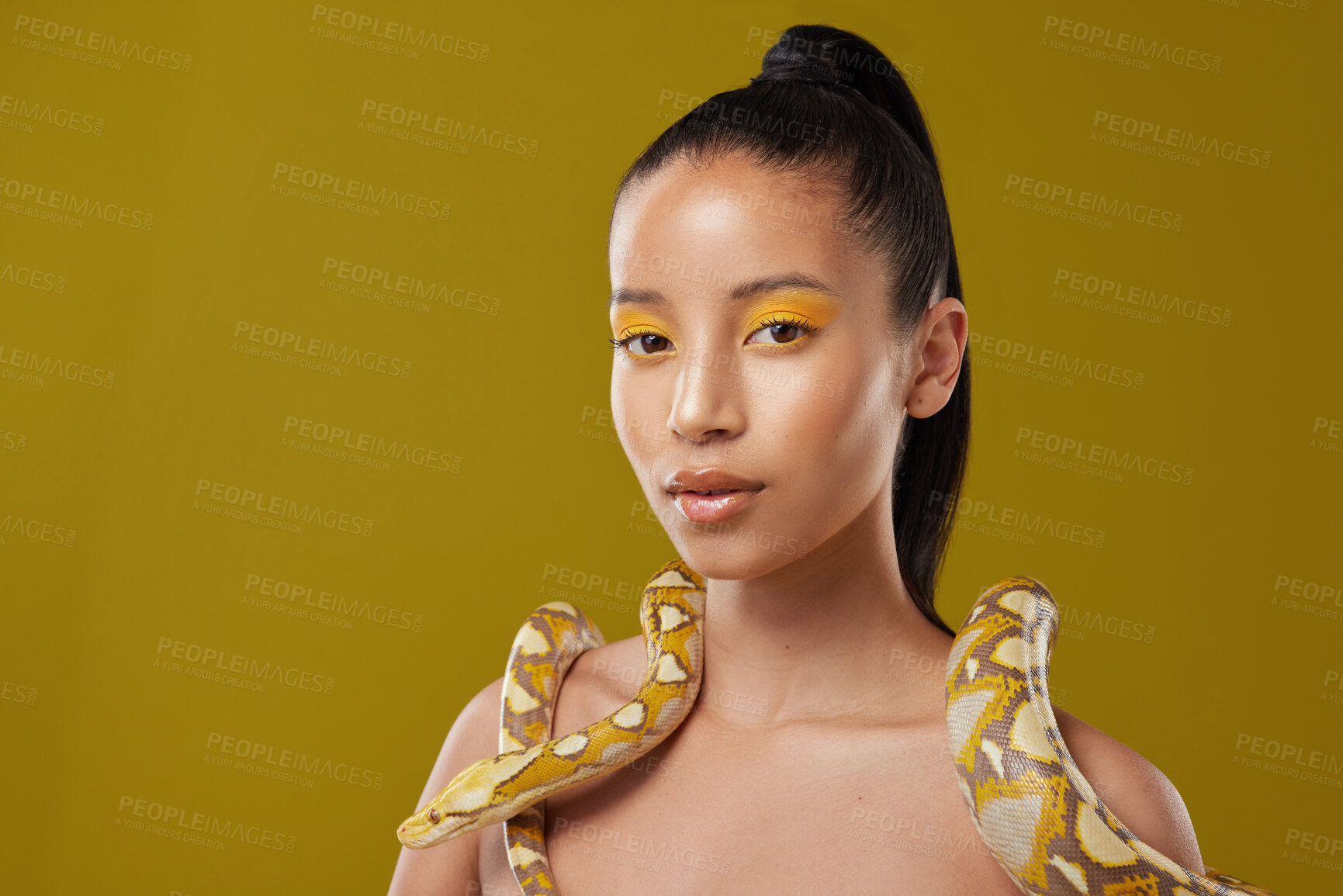 Buy stock photo Shot of a young woman posing with a snake around her neck against a yellow background