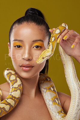 Buy stock photo Shot of a young woman posing with a snake around her neck against a yellow background