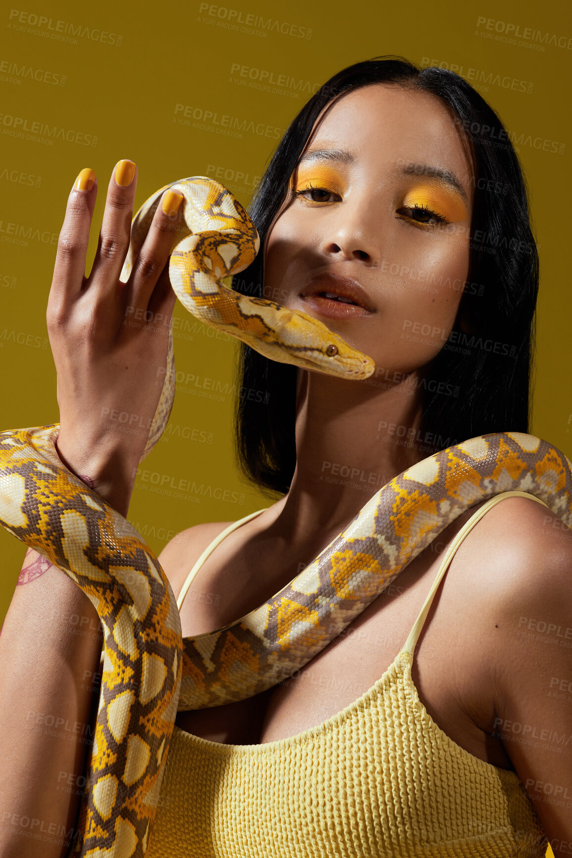 Buy stock photo Shot of a young woman posing with a snake around her neck against a yellow background