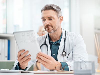 Buy stock photo Shot of a mature doctor working on a digital tablet in a medical office