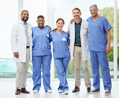 Buy stock photo Shot of a cheerful group of doctors standing with their arms around each other inside of a hospital during the day
