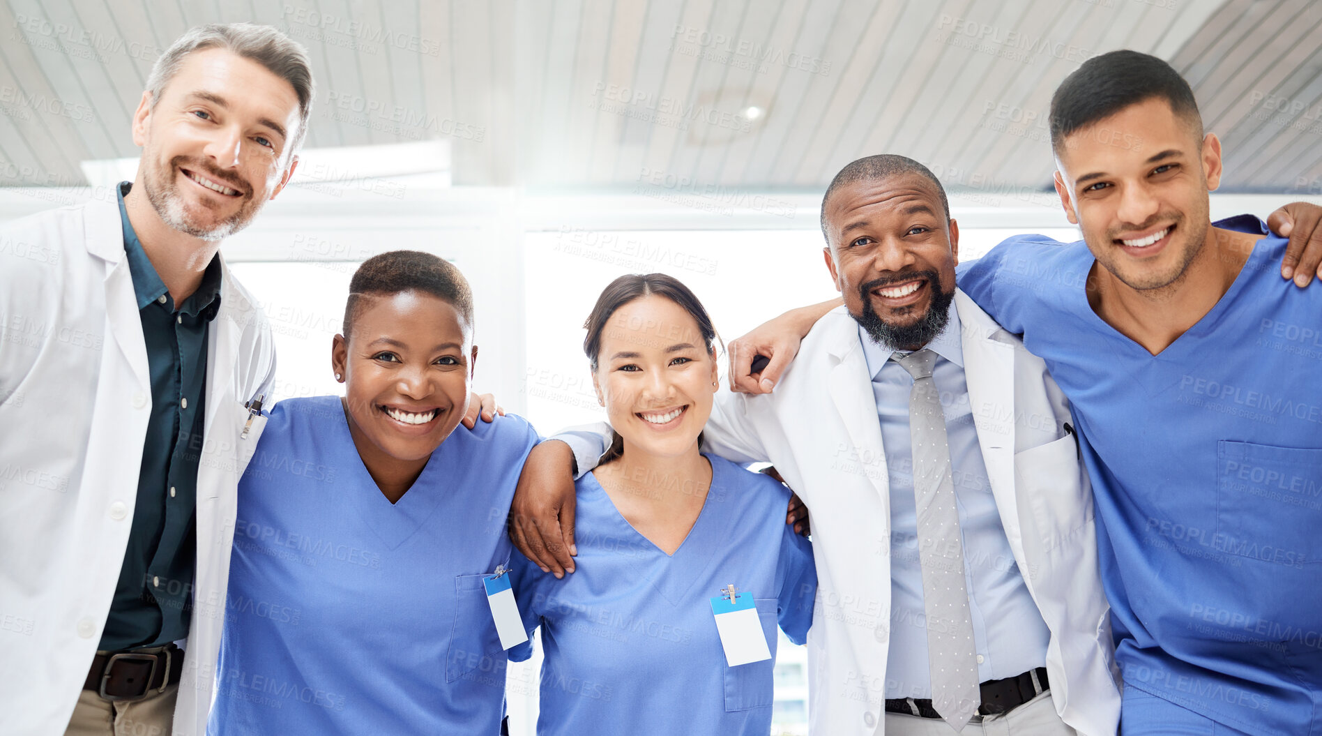 Buy stock photo Shot of a cheerful group of doctors standing with their arms around each other inside of a hospital during the day