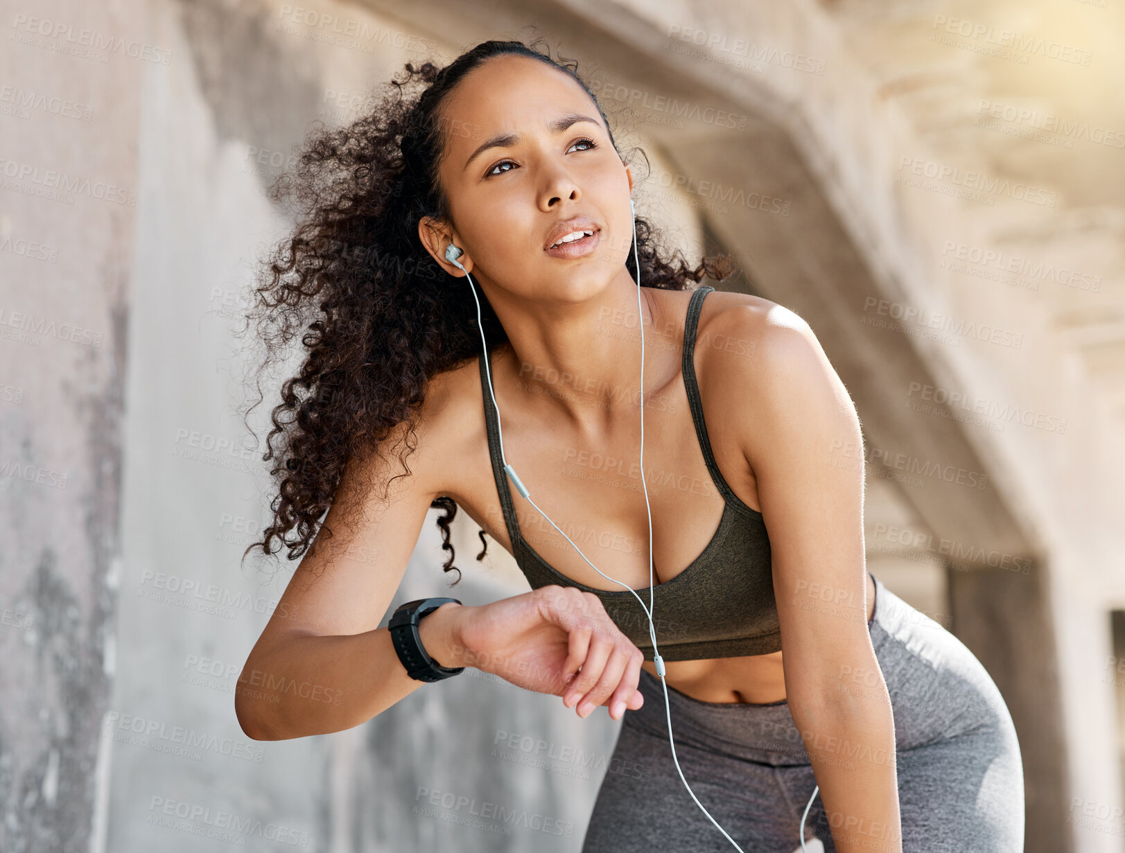 Buy stock photo Shot of an attractive young woman looking contemplative while checking her watch during her outdoor workout