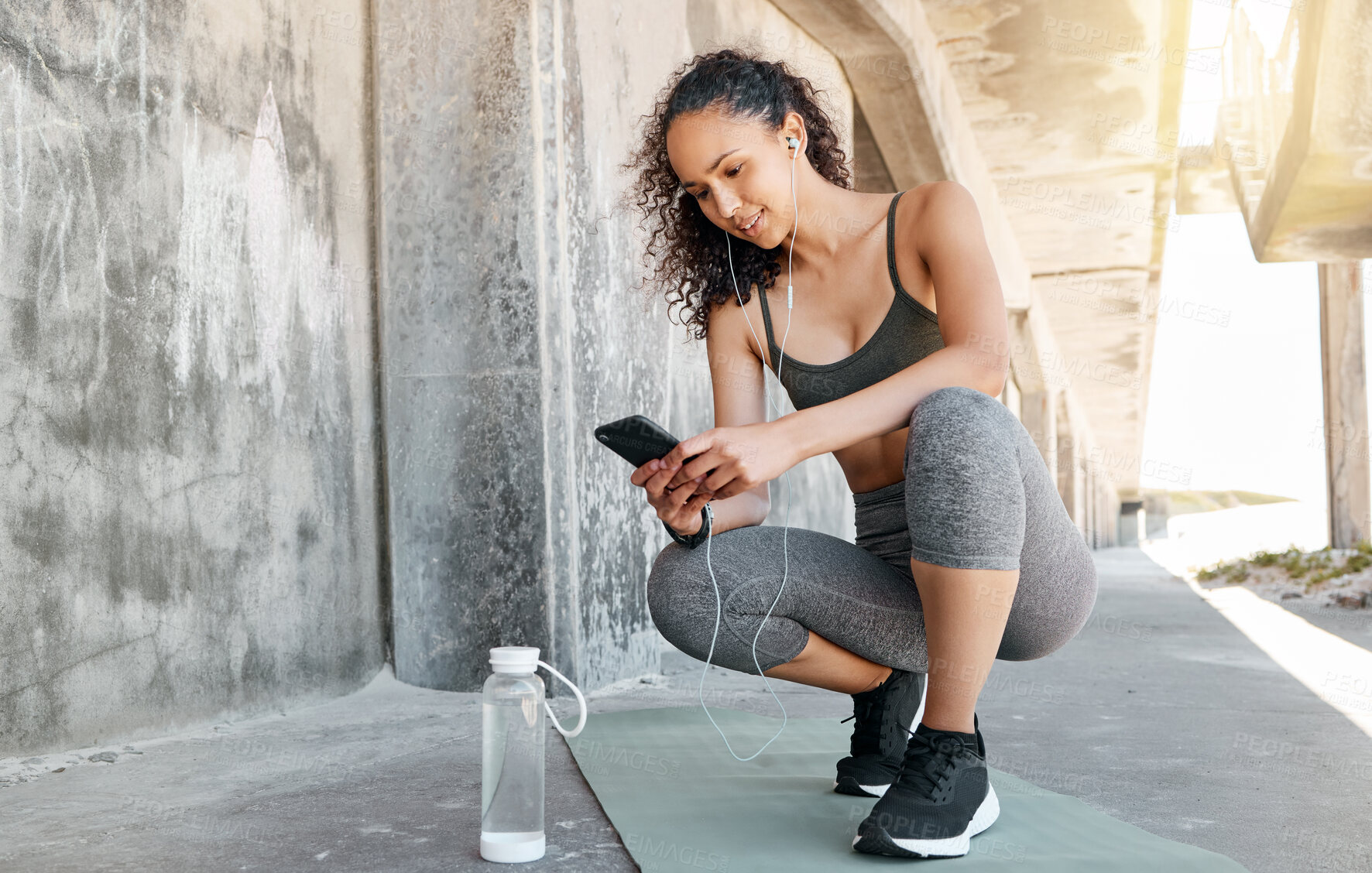 Buy stock photo Full length shot of an attractive young woman crouching down and using her cellphone during her outdoor workout