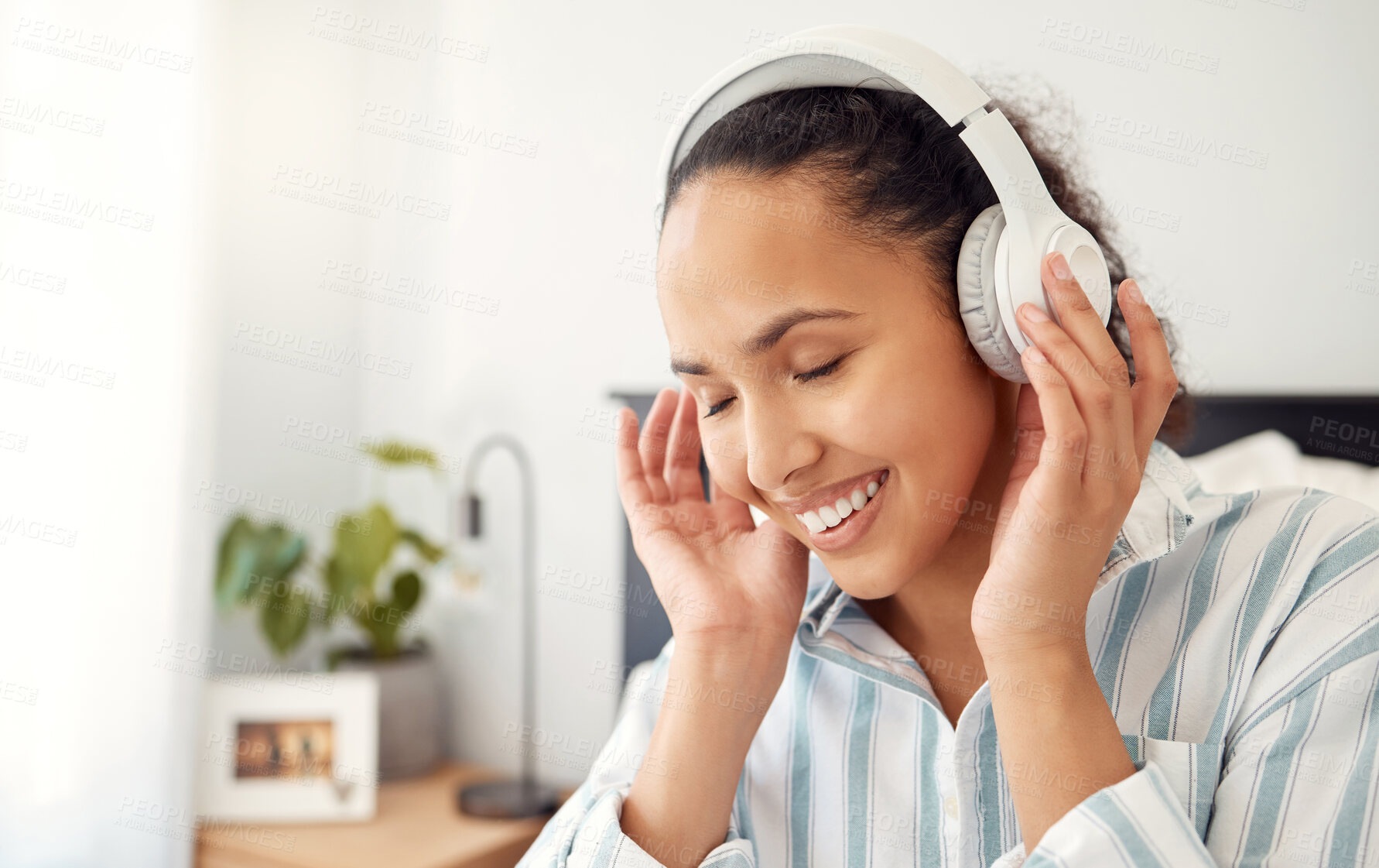 Buy stock photo Shot of a young woman listening to music while sitting on her bed at home