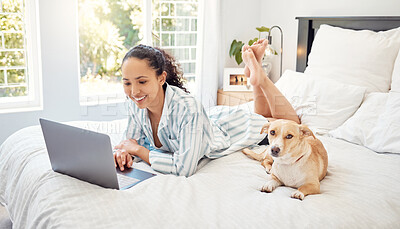 Buy stock photo Shot of a young woman using a laptop while relaxing on her bed at home