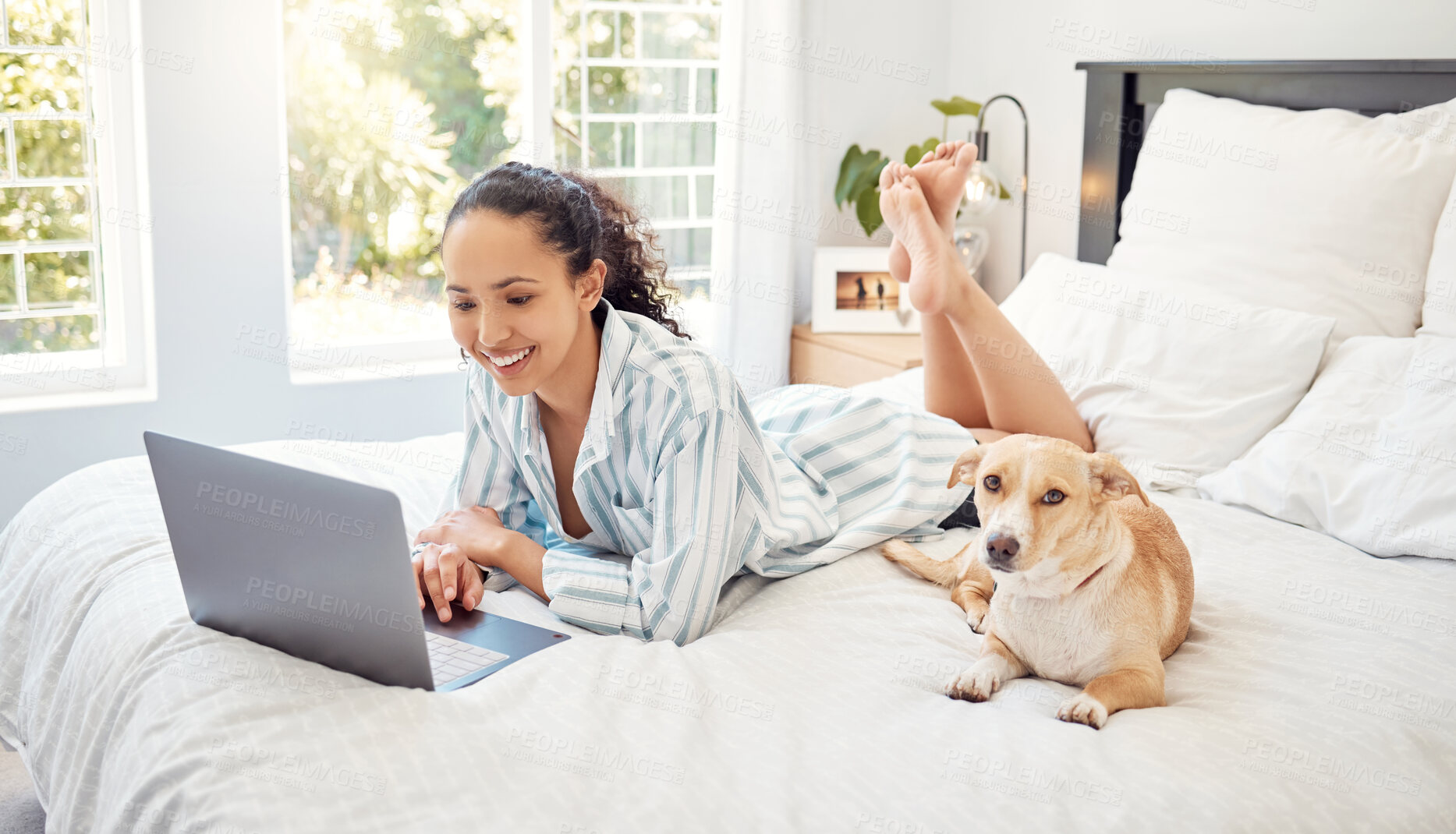 Buy stock photo Shot of a young woman using a laptop while relaxing on her bed at home