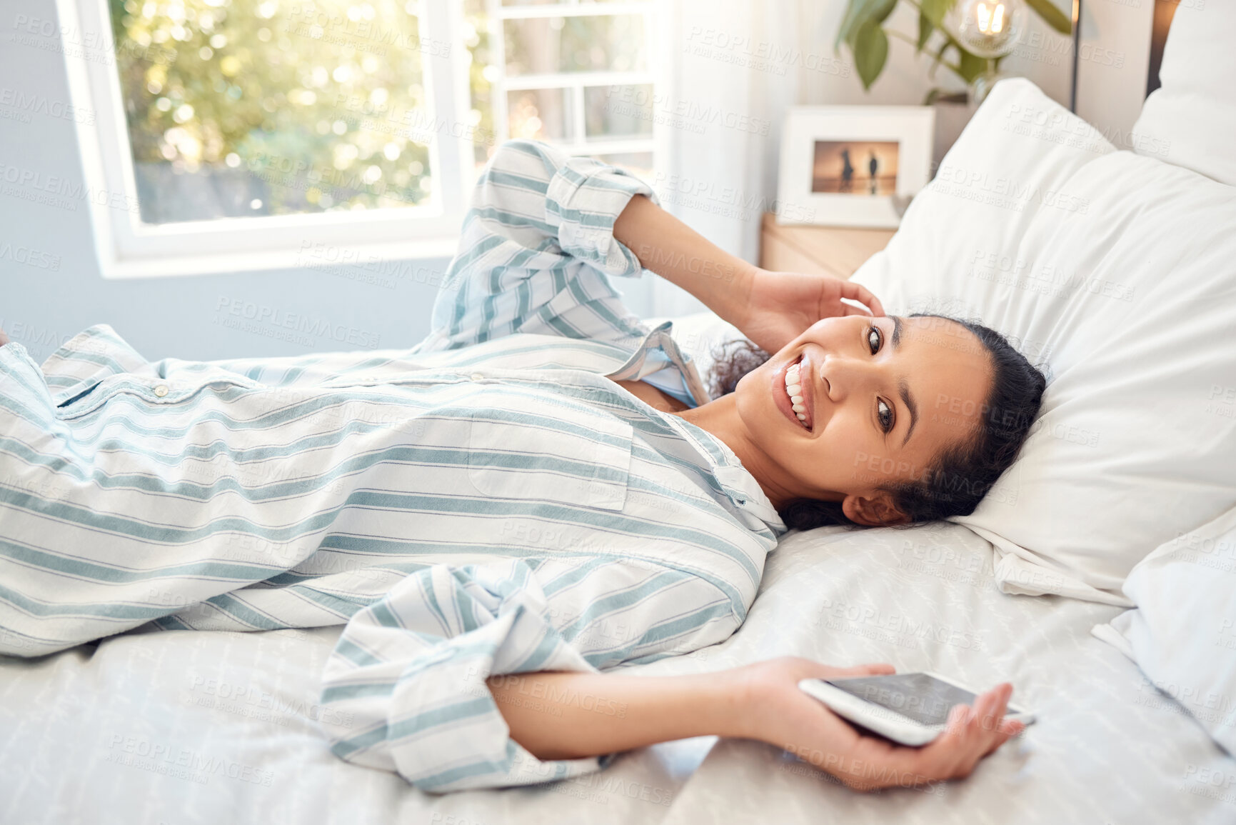 Buy stock photo Shot of a young woman using a phone while relaxing in bed at home