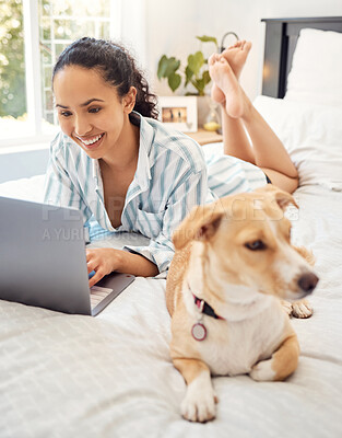 Buy stock photo Shot of a young woman using a laptop while relaxing on her bed at home