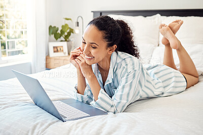 Buy stock photo Shot of a young woman using a laptop while relaxing on her bed at home