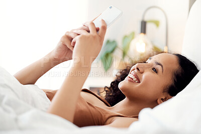 Buy stock photo Shot of a young woman using a phone while relaxing in bed at home