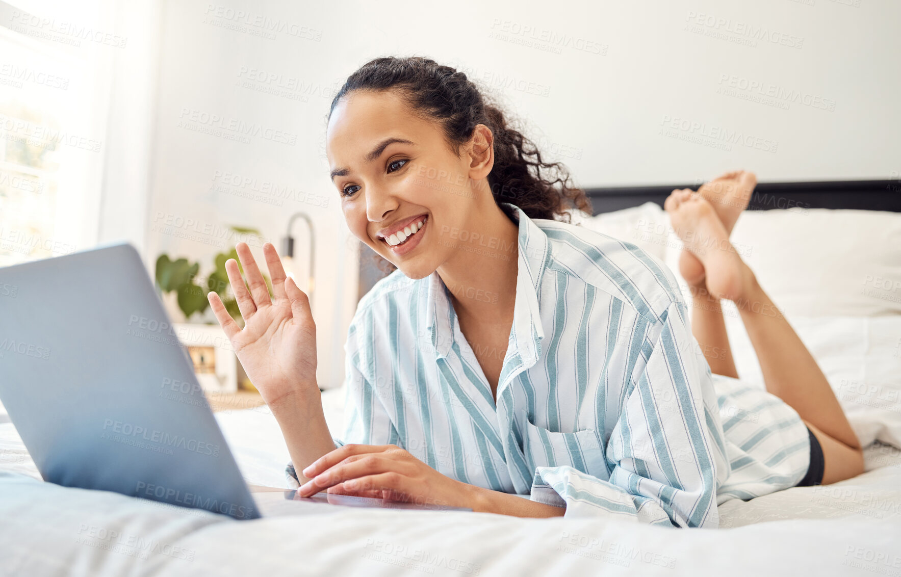 Buy stock photo Shot of a young woman using a laptop while relaxing on her bed at home