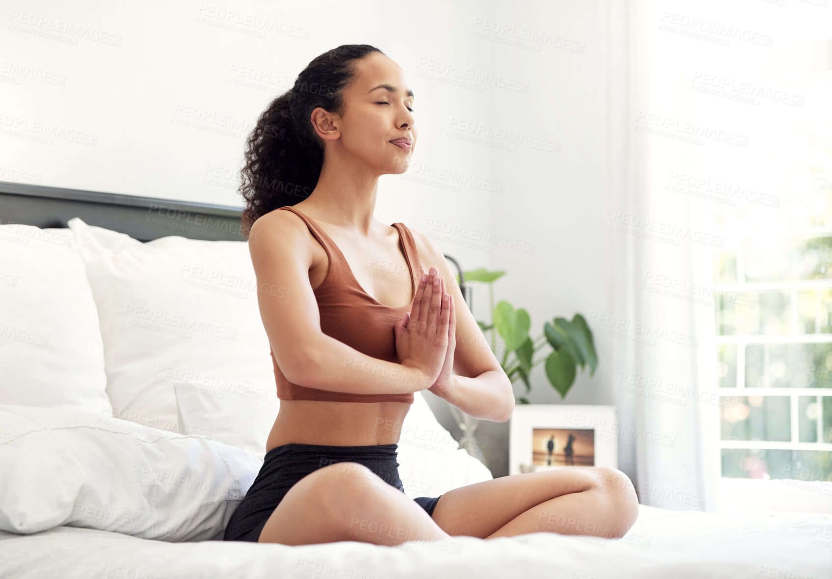 Buy stock photo Shot of a young woman praying while sitting on her bed at home