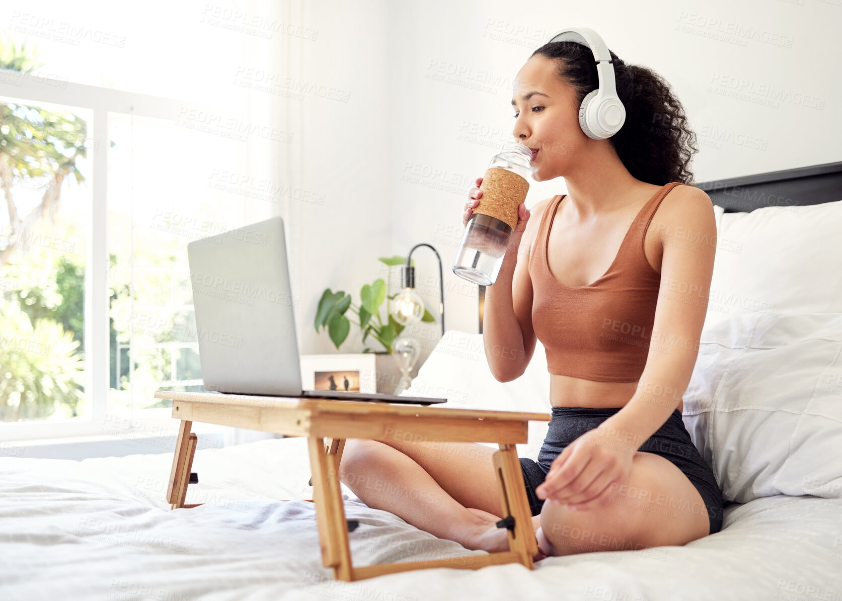 Buy stock photo Shot of a young woman using a laptop while sitting on her bed at home